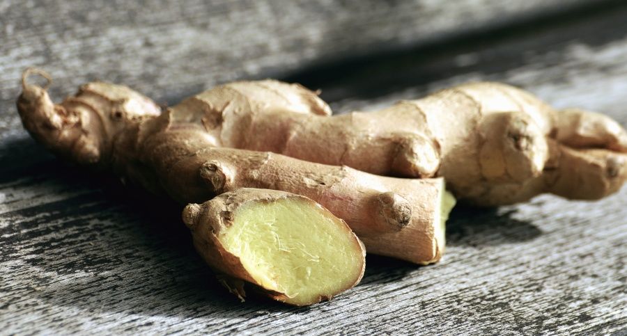 A plump ginger root on a wooden surface. It's been cut on one end to expose the pulp.