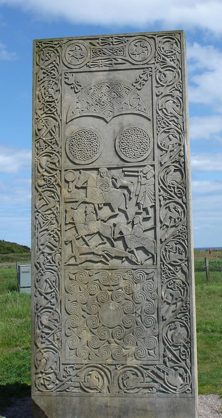 A grey stone slab carved with elaborate knotwork and spiral forms, as well as the shapes of horsemen.