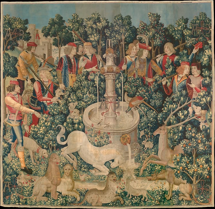 A woven tapestry showing a white unicorn at a fountain, plus other animals, trees, and a late medieval hunting party.