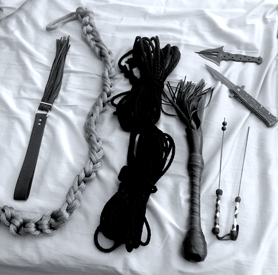 A black and white photo of a couple smaller hand floggers, three lengths of rope, and some sharp or pointy objects.