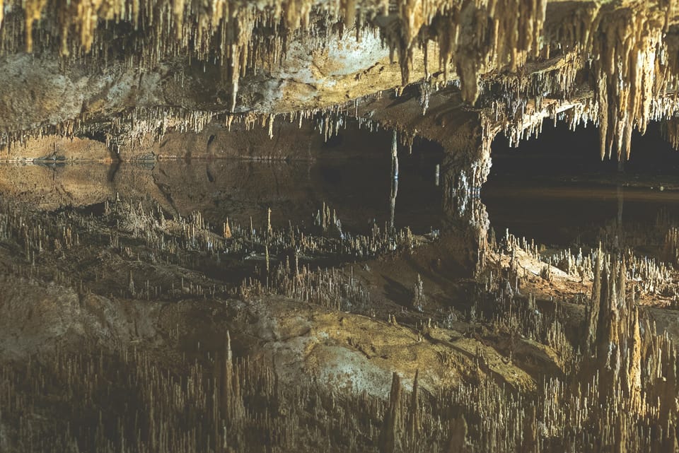 A cave interior riddled with stalactites on the ceiling, reflected perfectly by a pool below.
