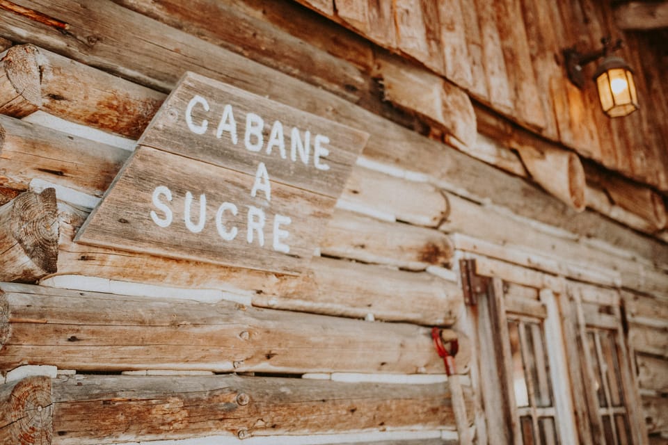 A log cabin exterior with a lantern over a doorway and a sign with the French phrase "cabane à sucre."